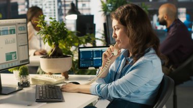 Ofisteki işçiler çizelgeleri incelerken sabit telefon kullanarak müşterilerle konuşuyorlar. İş yerinde çalışan iş ortağıyla konuşma, iş performans ölçümlerini analiz etme, kamera A