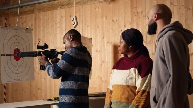 Atış poligonu güvenlik görevlisi, kurallara uymalarını sağlamak için yarı otomatik silahı müşterilere güvenli bir şekilde nasıl doldurulacağını gösteriyor. Atış poligonu çalışanı düzgün saldırı tüfeği kullanmayı öğretiyor, kamera A