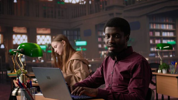 Black male student collecting academic information from the campus library, doing research to help with exam preparations. Pupil with education opportunity fights for a certificate. Camera B.