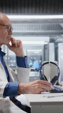 Modern laboratuardaki dikey video uzmanı deney verilerini beklerken kalemle oynuyor. Biyoteknoloji üzerine ileri tıbbi araştırmalar sırasında sabırsızlık ve endişe konsantrasyonunu yansıtıyor.