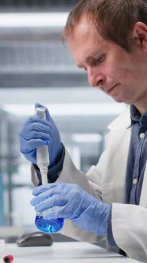 Laboratuvardaki araştırma çalışmaları sırasında madde taşımak için pipette kullanan dikey video uzmanı, kimyasal elementleri deney için karıştırıyor. Biyoteknoloji bilimsel çalışma ve yenilik