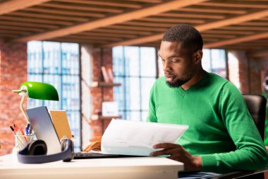 Muhasebe işinde çalışan bir adam, mali raporlara göz atıyor. Ekonomik grafikler ve rakamlar içeren, muhasebe görevlerini çözen uzak bir işçi