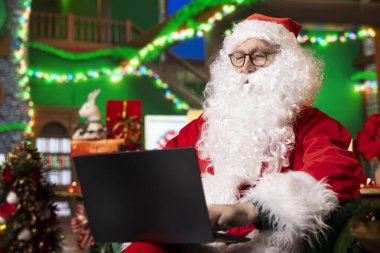 Noel Baba, dizüstü bilgisayarını güncellenmiş kızak aksesuarları için web sitelerini taramak için kullanıyor. Noel Baba şenlik atölyesinde yüksek teknolojili kızak ekipmanları arıyor.