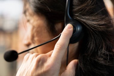 Kulaklık mikrofonuyla konuşan çağrı merkezi ajanı, müşteri aygıtlarına bağlanmak için uzaktan erişim araçları kullanıyor. Müşteri merkezi çalışanı, kulaklık kullanarak müşterilere kurulum konusunda yardım ediyor.