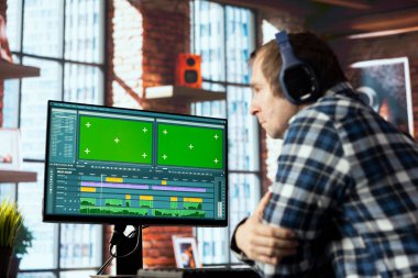 Video düzenleyici, video montajı yaparken kullanılacak anahtar çerçeveleri seçiyor, yeşil ekran bilgisayarda evden çalışıyor. Apartman ofisindeki video görüntülerini düzenlemek için fareyi kullanan adam.