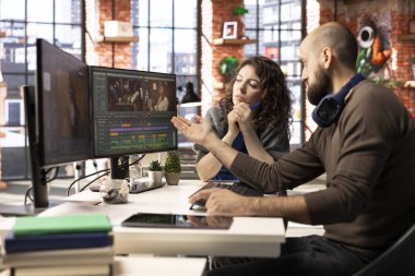 Erkek ve kadın film yapımcıları, yaratıcı bir video projesi için modern bir teknoloji kurulumu ve kurgu yazılımı kullanarak, post prodüksiyon için bir video çekimi düzenliyorlar. Çift monitörlü modern çalışma alanı.