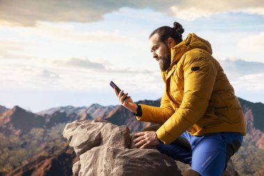 Erkek kaşif telefonunu dağın tepesinde gezdiriyordu, teknolojiye takıntılıydı ve her zaman internete bağlıydı. Genç yürüyüşçü manzaranın tadını çıkarıyor..