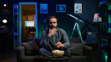 Şaşırmış yüz ifadesi olan bir adam TV 'de ilgi çekici programlar izliyor ve patlamış mısır yiyor. Ekrana yakından bakan kişi, şüpheli gerilim filmi izliyor, B kamerasını kapatın.