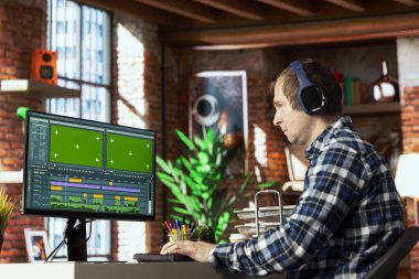 Video düzenleyici kulaklık takıyor, video montaj yapıyor, yeşil ekranda özel yazılım uygulaması kullanıyor. Evde Freelancer film projesinin görüntülerini kesmek için kurgu araçlarını kullanıyor