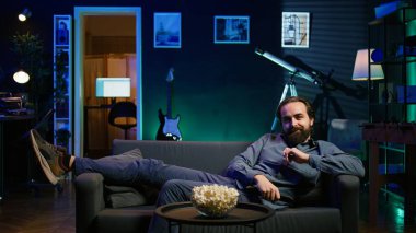 Heyecanlı adam kendini kanepeye atıyor, en sevdiği TV dizisinin ilk bölümüne yetişmek için acele ediyor. Evdeki kanepede zıplayan televizyon dizisini izlemek için sabırsızlanan hevesli insan, kamera B