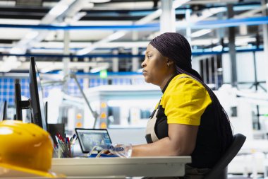 Photovoltaics fabrikası yöneticisi test denetimi için bilgisayarı kullanarak üretim sürecini inceliyor. Çevre dostu yenilenebilir enerji için güneş paneli yapılandırmalarını geliştiren kadın.