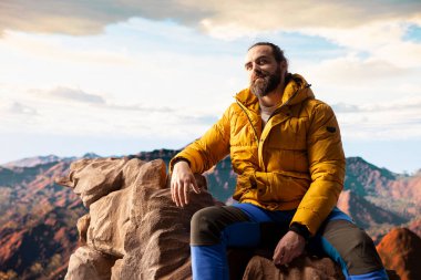 Gezgin, yüksek bir dağ sırasının kenarında tek başına duruyor, bulutlara ve çarpıcı panoramik manzaraya bakıyor. Memnun yürüyüşçü kişisel gelişim ve azim gösteriyor.