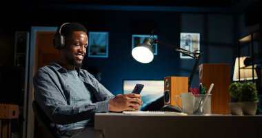 Siyah uzaktan kumandalı işçi, cep telefonu uygulamalarına kaymak için ara veriyor, mesajlaşıyor ve arkadaşlarıyla çevrimiçi sohbet ediyor. Genç serbest çalışan adam birden fazla iş yapmaktan hoşlanıyor, müzik dinliyor. Kamera A.