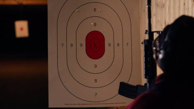 Atış taliminde tabancalı bir kadın, kağıttan hedefle ilgili sonuçlara bakıyor. Afrikalı Amerikalı atıcılık sporu yapıyor, keskinleştirme becerileri, kontrol noktaları tam 12 'den, kamera B' den.
