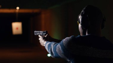 Atış talimi yapan gülümseyen bir adamın portresi, düzgün silah tutmayı ve eğlenmeyi öğrenmek. Neşeli silah meraklısı, silahlı, koruyucu gözlüklü, B kameralı.