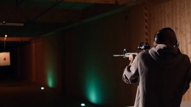 Atış poligonu müşterisi yarı otomatik silahla hedefleri vuruyor, eğleniyor. Kapalı alanda ateş eden bir adam boğa güreşçilerine tüfekle ateş ediyor, koruma ekipmanları takıyor, kamera A