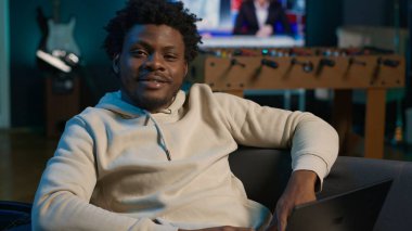 Gülümseyen erkek serbest çalışan modern bir dairede dizüstü bilgisayarla internette geziniyor. Bağımsızlığın yaşam tarzını gösteriyor. Sanal bir çalışma alanında verimlilik, birden fazla iş. Kamera A.