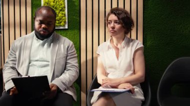 Afrika kökenli Amerikalı iş arayan, iş görüşmesi için İK bürosundaki kadından sonra aranmayı bekliyor. Koridorda elinde evrakları ve özgeçmişiyle bekliyor. Adayları çağırın. Kamera A.