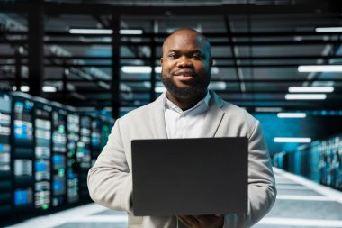 Depolama dizilerini etkileyen, yedekleme yapan ağ sorunlarını çözmek için laptop kullanan iyimser sunucu merkezi yöneticisinin portresi. Veri merkezindeki neşeli adam sistem testleri yapıyor, termal seviyeleri izliyor.