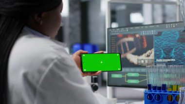 Akıllı telefon üzerinde laboratuvar çalışması için krom anahtar ekranı kullanan siyah bir uzman moleküler bilim için deney verileri üzerinde çalışıyor. Gelişmiş araştırma, farmakoloji ve biyoteknoloji keşfi. Kamera B.