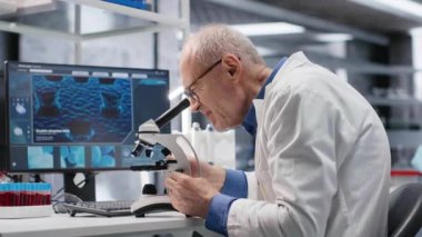 Mikroskop altında numuneleri inceleyen yaşlı bir bilim adamıyla laboratuvar. Klinik deneyler, biyoloji, patoloji ve yenilik için yapılan moleküler araştırmaların keşif sürecini göstermektedir. Kamera B.