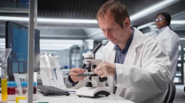 Laboratuvarda araştırma çalışması için mikroskop altında numune tepsisi inceleyen çalışanlar hücresel araştırmayı kaydırıyor ve genetik araştırmayı destekliyor. Sağlık hizmetleri için gelişmiş analiz. Kamera A.