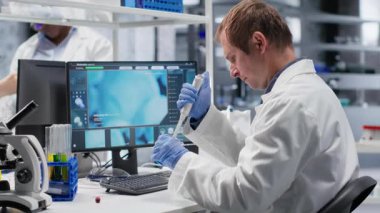 Erkek bilim adamı, laboratuarda işlem sırasında pipeti kavanozun üzerine damlatarak tutar. Genetik araştırmaları, nanoteknoloji ve çözümleri analitik yöntemlerle destekleyen karışım hazırlığı. Kamera B.