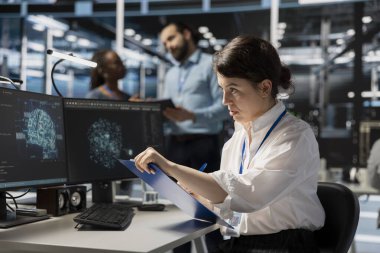 Sunucu odası çalışanı Yapay Zeka görselleştirme çizelgelerine bakıyor, denetimden önce panodaki belgeleri inceliyor. Yapılandırma verilerini ve masa başındaki uyum standartlarını doğrulayan yapay zeka veri merkezi uzmanı