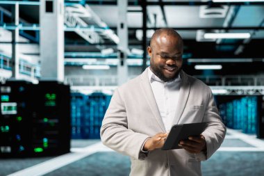 Happy Veri Merkezi Mühendisi tablet üzerinde çalışan kod satırları yazıyor. Sunucu odasındaki aygıtta programlama betikleri kullanan neşeli bilişim uzmanı