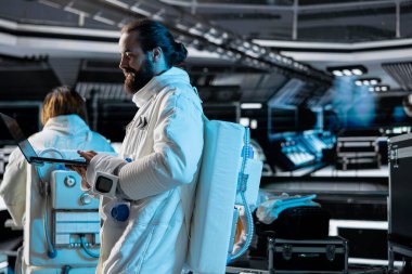 Bilimsel araştırmaları koordine eden fütürist uzay aracının içinde astronot kıyafeti giyiyor. Astronot ekipman ile uzay yolculuğu keşif görevi için hazırlanıyor not defterinde metrik kullanarak