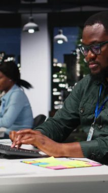 Dikey Video Siyah çalışma arkadaşları karanlık ofisteki yeni bir aylık analiz için tahmin verilerini izleyerek rapor ve açıklamaları planlamak için raporları ve görüşleri kullandılar. Saatler sonra gol atılacak. Kamera.