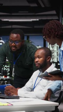 Dikey Video Afrikalı Amerikalı çalışanlar aylık raporlar için birbirlerine danışıyorlar, gece geç saatlerde iş verimliliği için KPI veri içgörülerini gözden geçiriyorlar. Çalışanlar arasındaki işbirliği