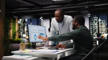 Afrika kökenli Amerikalı işçiler geceleri görev çözmede birbirlerine danışırlar, aylık raporları tamamlarlar ve verimlilik için KPI verilerini incelerler. Başarı için işbirliği. Kamera A.