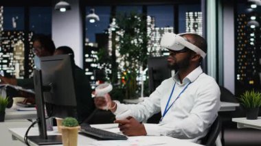 Genç siyah işadamı sanal gerçeklik kulaklığı ve diğer cihazları kullanarak bir strateji oluşturuyor, öngörülerde bulunuyor ve başarı için risk değerlendirmesini belgeliyor. İş hedefleri. Kamera B.