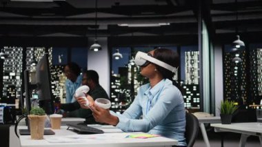 Afrika kökenli Amerikalı bir kadın AI cihazını karanlık ofiste sanal gerçeklikle kullanıyor. Projeksiyonların doğruluğunu kontrol etmek ve analiz etmek için şirketin çalışma alanında VR gözlükleriyle fazla mesai yapıyor. Kamera A.