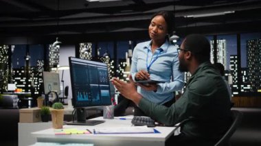 Afrika kökenli Amerikalı işçiler geceleri görev çözmede birbirlerine danışırlar, aylık raporları tamamlarlar ve verimlilik için KPI verilerini incelerler. Başarı için işbirliği. Kamera A.