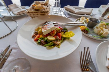 fresh vegetable salad with feta cheese and olives and tomatoes or green salad leaves on a plate on a table in a restaurant, close-up shot
