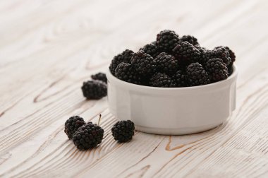 Blackberries in bowls on a light background on a wooden table, close-up shot