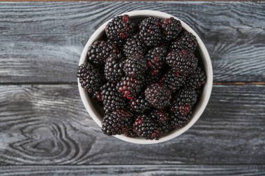 Ripe blackberries in a plate, close-up from above, vitamins on a dark wooden table, antioxidants and vitamins
