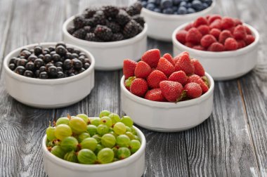 Fresh berries in six bowls - blueberries, blackberries and black currants, sweet cherries, blueberries on a wooden background. Fruit berry background.