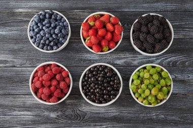 bowls with wild berries, raspberries, blueberries, blackberries, strawberries and gooseberries on a rustic wooden background