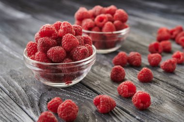 Ripe raspberries and scattered berries in glass saucers on a dark table background, close-up shot