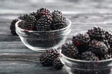 Ripe blackberries in glass saucers on a dark table background, close-up shot