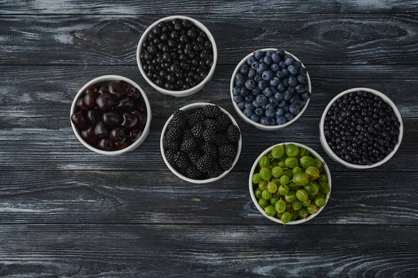 Ripe berries in bowls - blueberries, blackberries and black currants, sweet cherries, blueberries on a dark wooden background. dietary antioxidants and vitamins