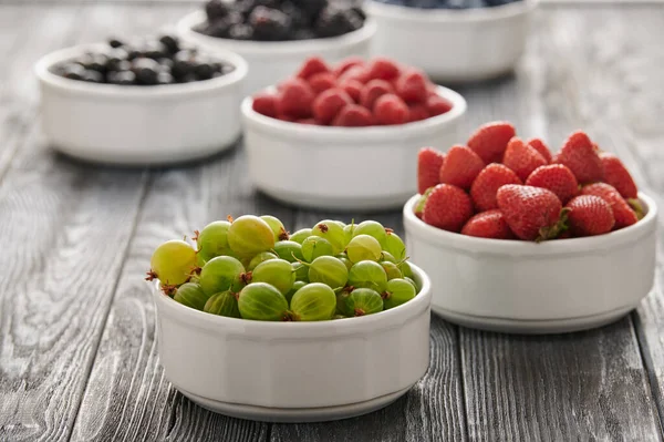 bowls with wild berries, raspberries, blueberries, blackberries, strawberries and gooseberries on a rustic wooden background