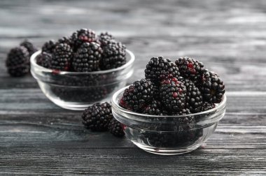 Ripe blackberries in bowls on a wooden table, close-up shot