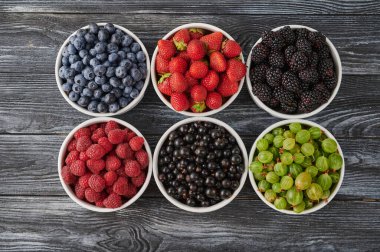 Fresh berries in six bowls - blueberries, blackberries and black currants, sweet cherries, blueberries on a wooden background. Fruit berry background.