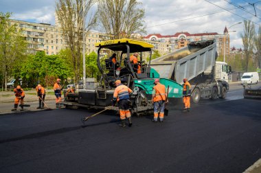 Bir grup yol işçisi ellerinde kürek ve kaldırım onarımı ile yolun bir kısmını asfalt ve yol inşaatı ile dolduruyorlar.