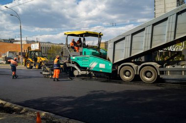 Bir grup yol işçisi ellerinde kürek ve kaldırım onarımı ile yolun bir kısmını asfalt ve yol inşaatı ile dolduruyorlar.