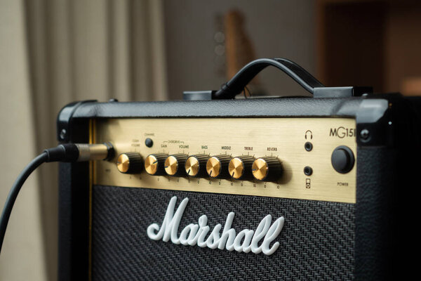 Carrara, Italy - May 2, 2023 - Marshall guitar amplifier with jack plugged in and a guitar on background. Shallow depth of field.